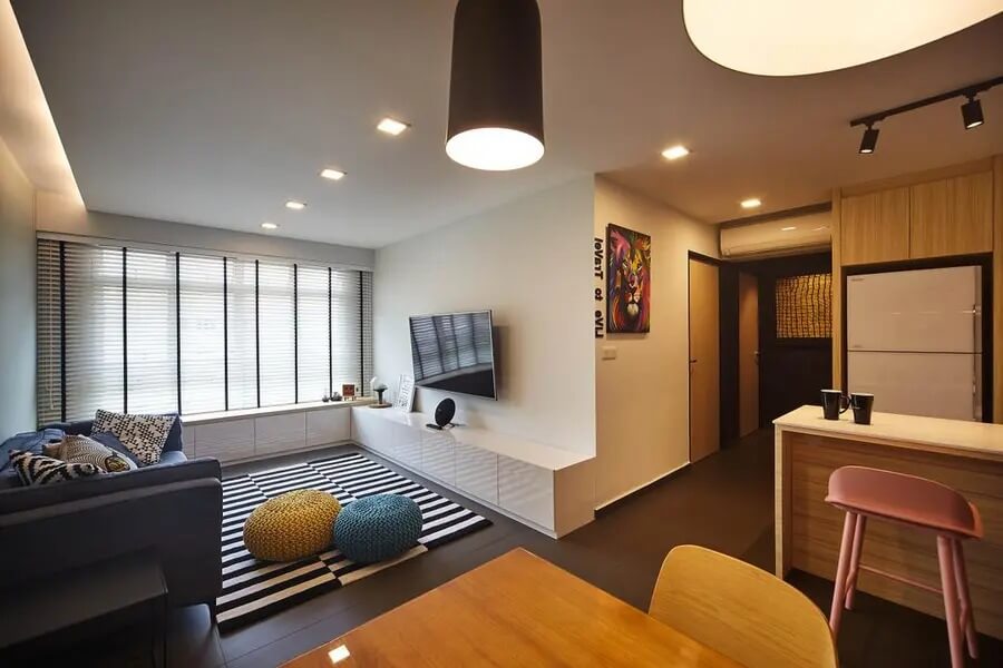 Phòng khách hiện đại với sofa, TV treo tường, thảm sọc trắng đen, và đèn treo. Không gian sáng và thoáng đãng.