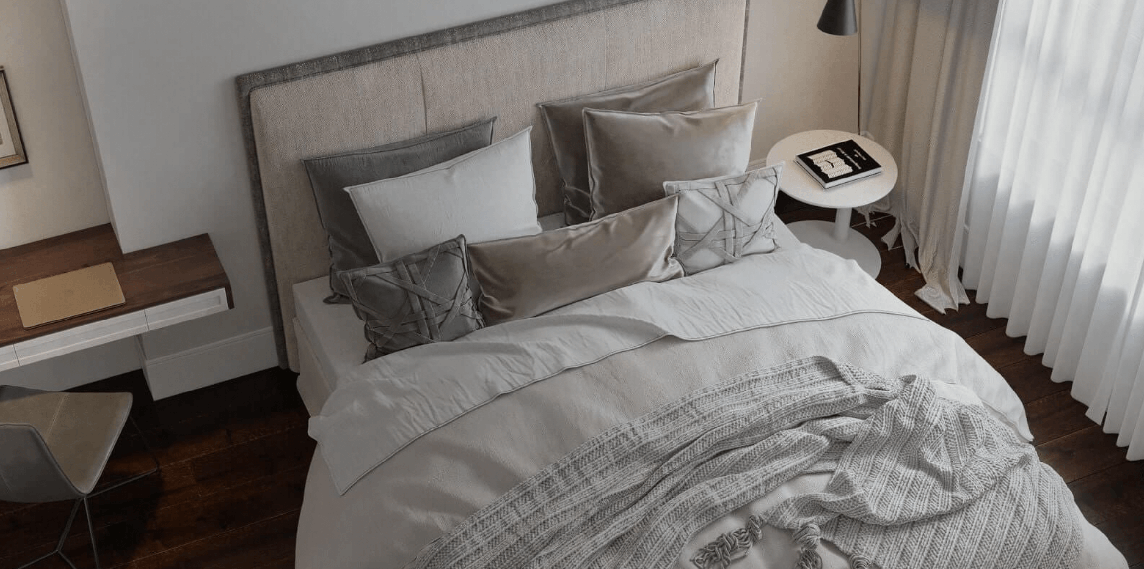 Giường ngủ sang trọng với ga gối màu xám, bàn làm việc nhỏ bên cửa sổ có rèm voan trắng.