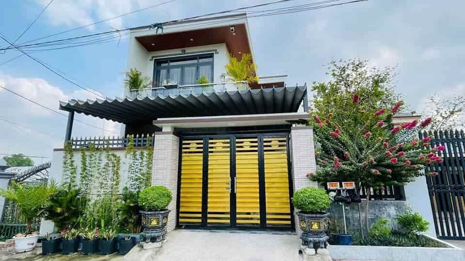 Nhà mái bằng hiện đại với cửa màu vàng và cây cảnh xanh tươi trước sân, trời trong xanh.