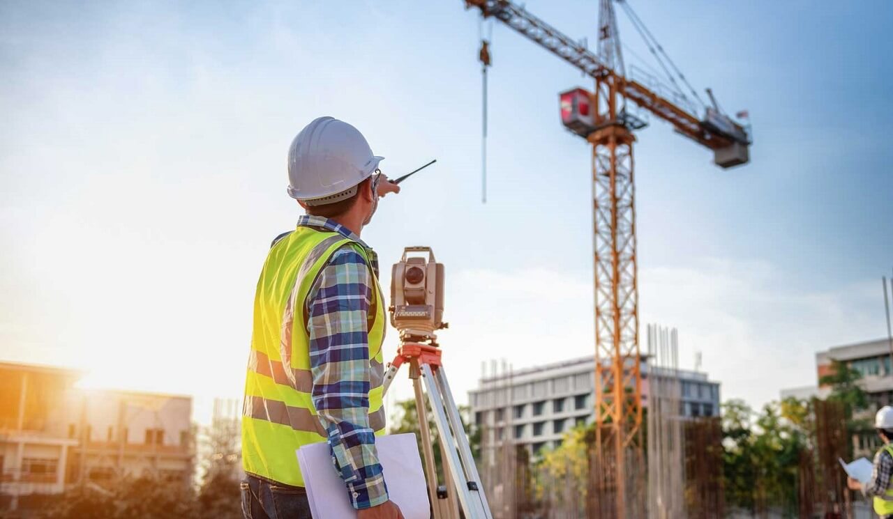 Kỹ sư xây dựng kiểm tra dự án tại công trường, với cần cẩu phía sau, khi hoàng hôn.