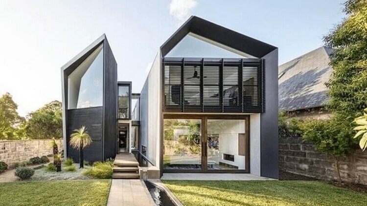 Ngôi nhà hiện đại với thiết kế mái chéo độc đáo, cửa sổ kính lớn và sân vườn xanh tươi.