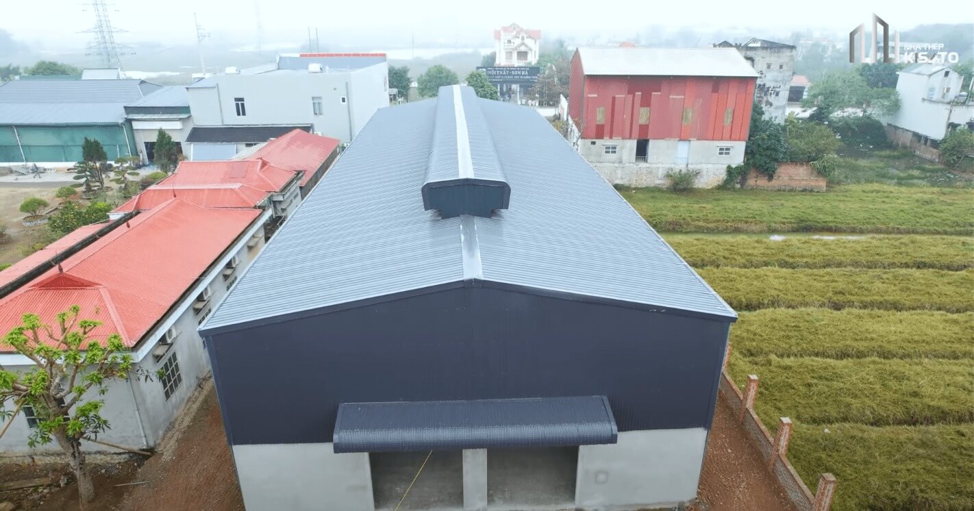 Nhà kho lớn màu xanh đậm nằm giữa đồng cỏ, bên cạnh các tòa nhà có mái đỏ ở vùng nông thôn.