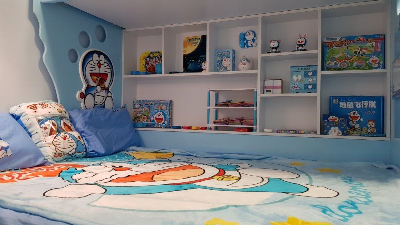 Phòng ngủ trẻ em trang trí chủ đề Doraemon với chăn, gối và kệ sách đầy màu sắc.