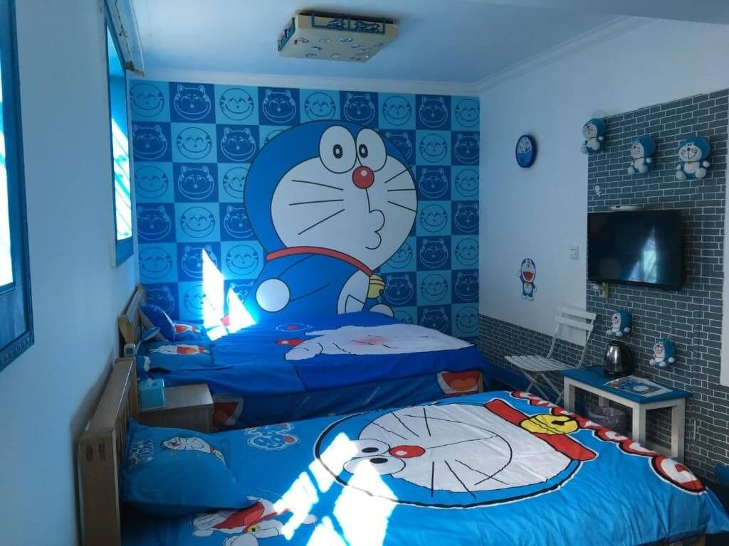 Phòng ngủ trang trí chủ đề Doraemon với giường và giấy dán tường hình Doraemon xanh nổi bật.