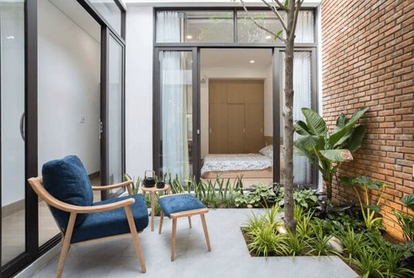 Khu vườn nhỏ ngoài trời với ghế xanh và nhiều cây xanh bên cạnh phòng ngủ sáng sủa.