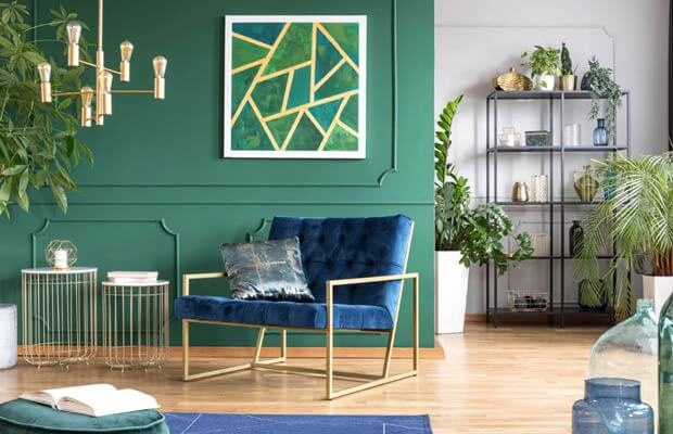 Phòng khách hiện đại với ghế nhung xanh, tường xanh lá, tranh treo tường và cây xanh trang trí, tạo không gian thư giãn.