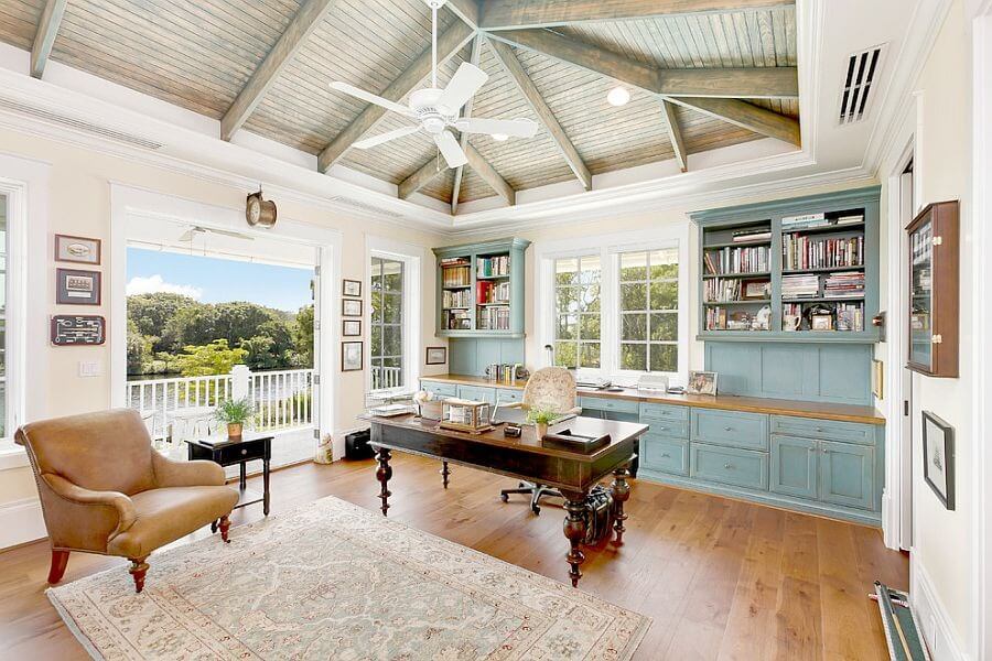 Văn phòng tại gia sáng sủa với bàn gỗ, ghế bành, kệ sách, trần gỗ và cửa sổ lớn nhìn ra quang cảnh xanh.