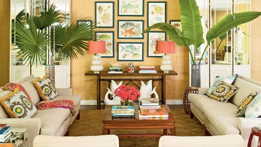 Phòng khách trang trí nhiệt đới với cây xanh, tranh nghệ thuật, gối họa tiết màu sắc và đèn bàn lớn.