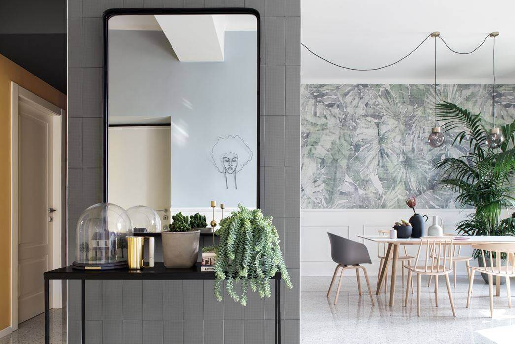 Nội thất phòng ăn hiện đại với bàn ghế gỗ, cây xanh và gương lớn, tường trang trí họa tiết lá.