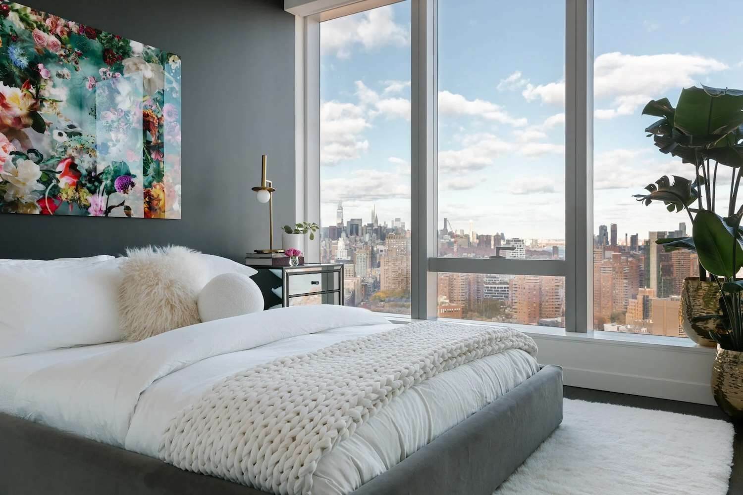 Phòng ngủ hiện đại với cửa sổ kính lớn, trang trí hoa nổi bật và tầm nhìn ra thành phố.