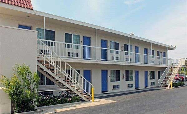 Nhà nghỉ hai tầng với cửa màu xanh, cầu thang bên ngoài, không gian thoáng đãng và bầu trời trong xanh.