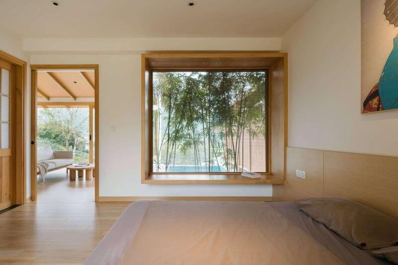 Phòng ngủ với cửa sổ nhìn ra vườn tre, nội thất gỗ hiện đại và ánh sáng tự nhiên.