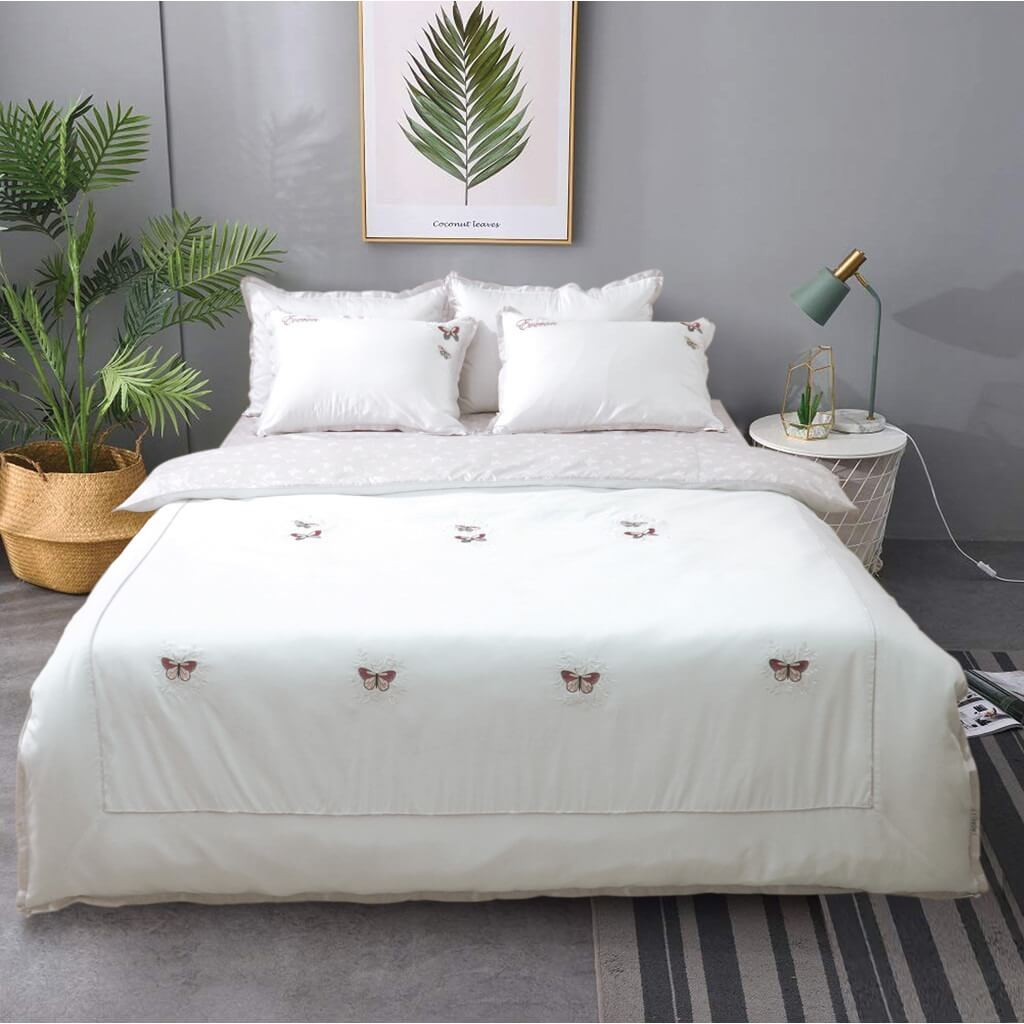 Giường ngủ trang nhã với chăn gối màu trắng, trang trí bướm, tường xám và cây xanh tạo không gian thư giãn.