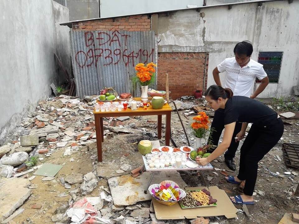 Người chuẩn bị bàn thờ cúng trong khu đất trống với nhiều món lễ vật và hoa.