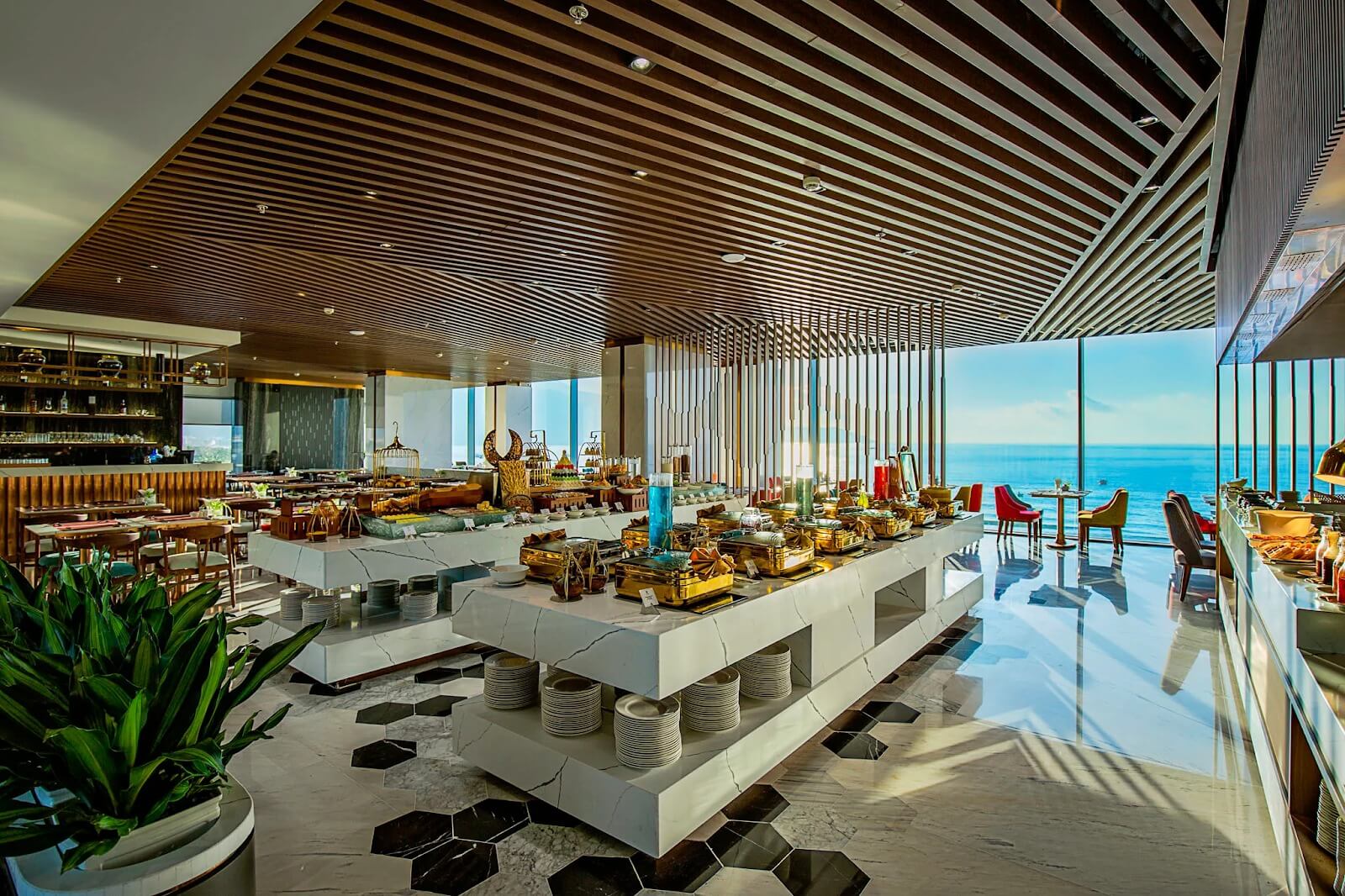 Nhà hàng buffet sang trọng với cửa sổ nhìn ra biển, bàn ăn đầy món ngon đa dạng.