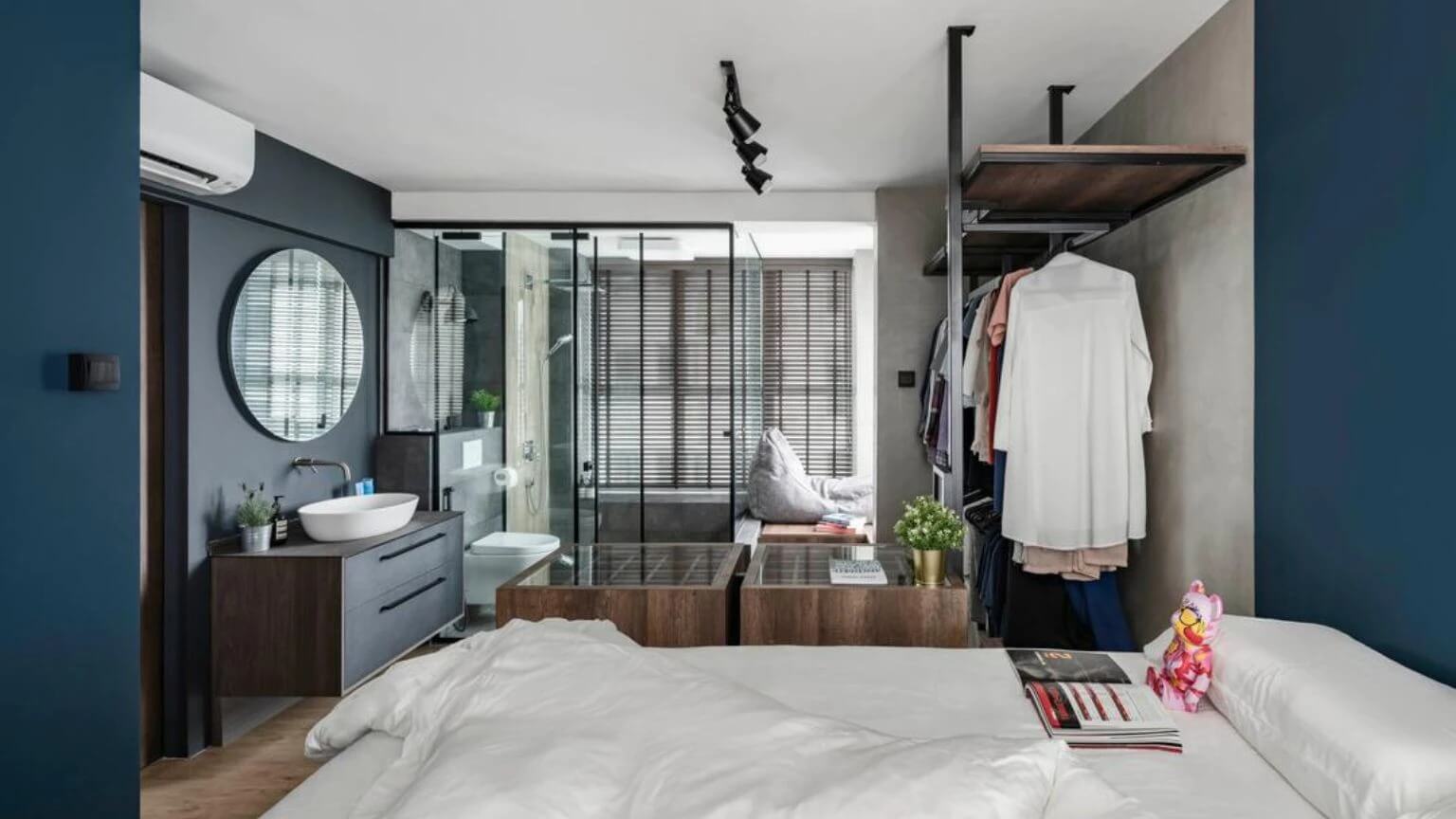 Phòng ngủ hiện đại với phòng tắm kính, giường trắng, tủ quần áo mở và bức tường xanh đậm.