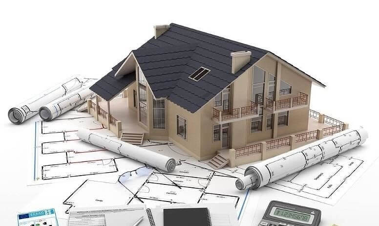 Mô hình nhà trên bản vẽ kiến trúc với ống cuộn và máy tính, thể hiện ý tưởng thiết kế xây dựng.