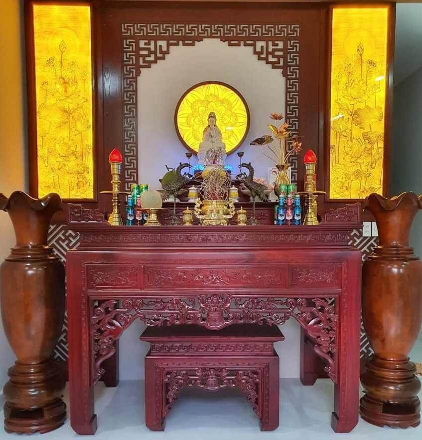 Bàn thờ gia tiên bằng gỗ với tượng Phật và nến đỏ, thiết kế trang trí truyền thống, mang màu sắc ấm áp.