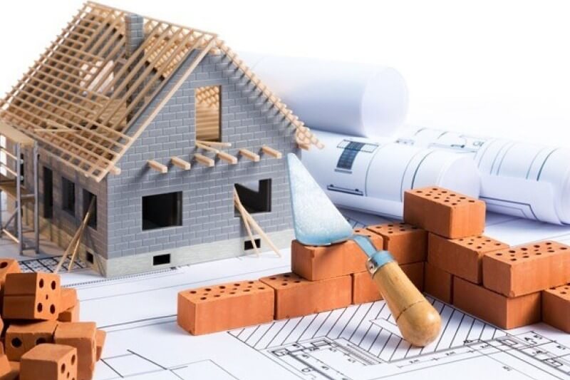 Mô hình ngôi nhà với gạch, bản vẽ kỹ thuật và bay xây dựng trên bàn, tượng trưng cho quá trình xây dựng.