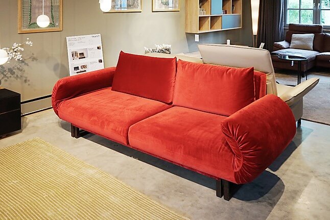 Sofa nhung đỏ sang trọng trong phòng khách hiện đại với ánh sáng tự nhiên và thảm vàng.