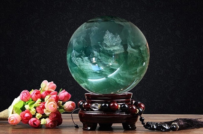 Quả cầu đá phong thủy màu xanh đặt trên đế gỗ cạnh bó hoa hồng, tạo cảm giác huyền bí và sang trọng.