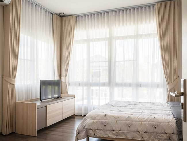 Phòng ngủ hiện đại với giường, rèm cửa ánh sáng tự nhiên, tủ TV gỗ sáng, mang lại không gian thoải mái và thoáng mát.