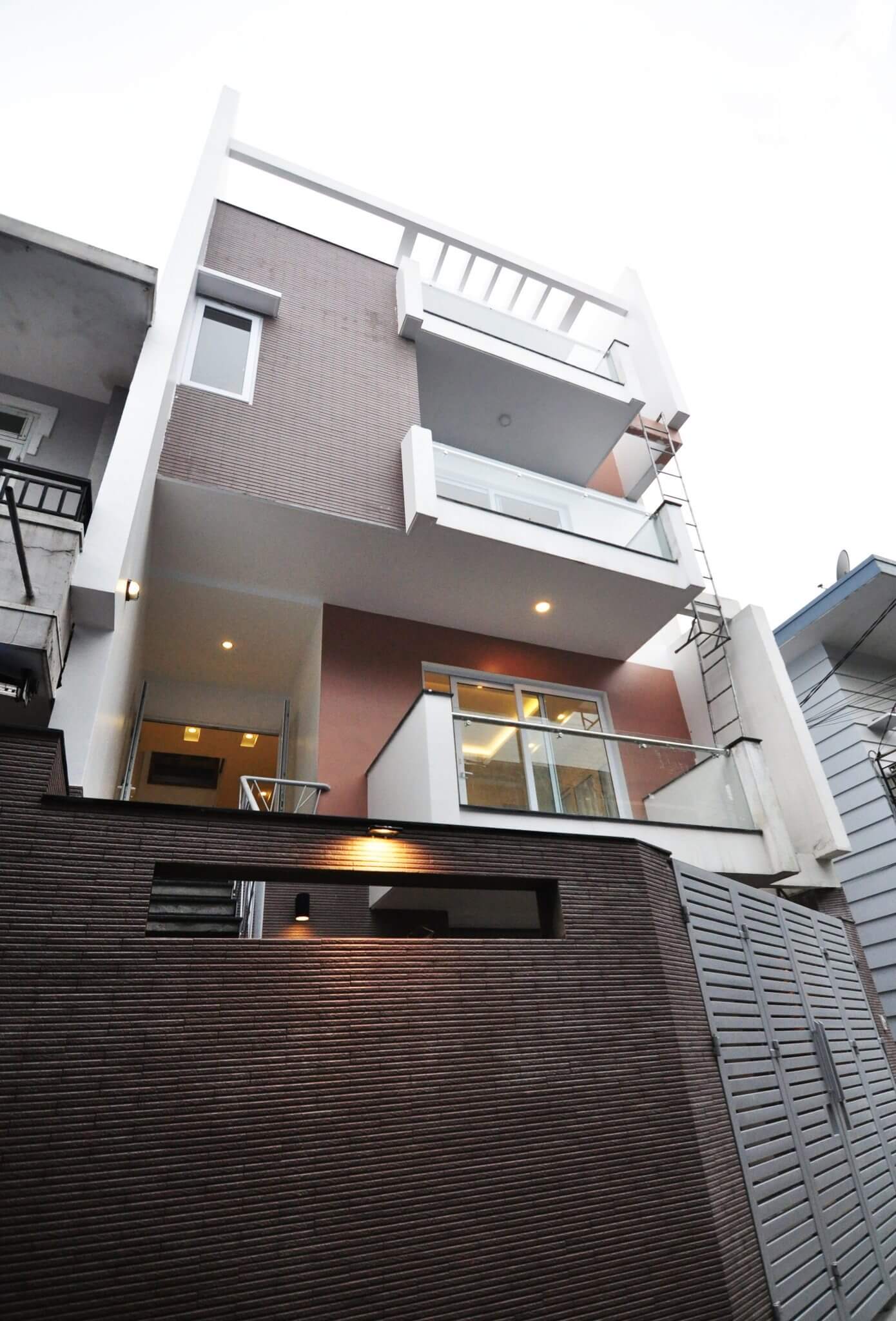 Ngôi nhà hiện đại ba tầng với ban công kính và tường gạch, phong cách kiến trúc độc đáo.