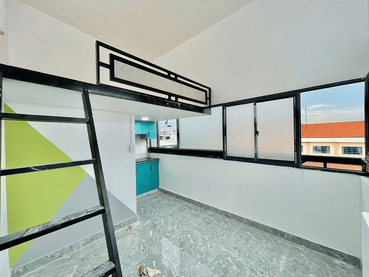 Căn phòng nhỏ gọn với gác lửng, cửa sổ lớn và thiết kế nội thất hiện đại, sáng sủa và tối giản.