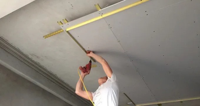 Người đàn ông đang lắp đặt trần thạch cao với máy khoan điện trong một công trình xây dựng.