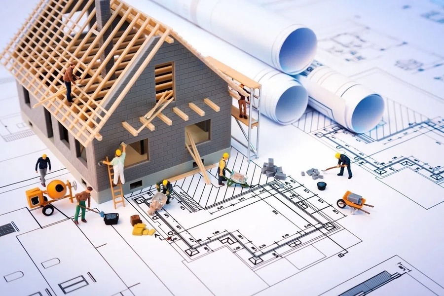 Mô hình công trình xây dựng trên bản vẽ thiết kế kiến trúc, có công nhân mini và thiết bị xây dựng.