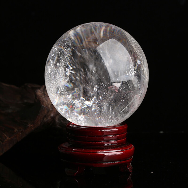 Quả cầu pha lê đặt trên đế gỗ đỏ, phản chiếu ánh sáng lấp lánh trong không gian tối.