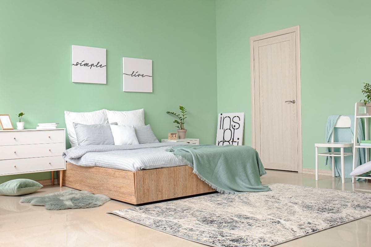 Phòng ngủ hiện đại với tường xanh pastel, giường gỗ, tranh treo và thảm nhã nhặn.