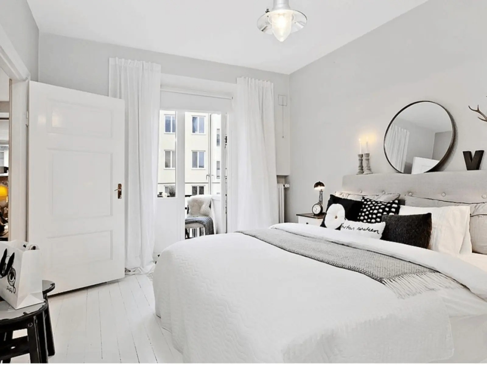 Phòng ngủ hiện đại với giường màu trắng, gối trang trí và ánh sáng tự nhiên từ cửa kính.