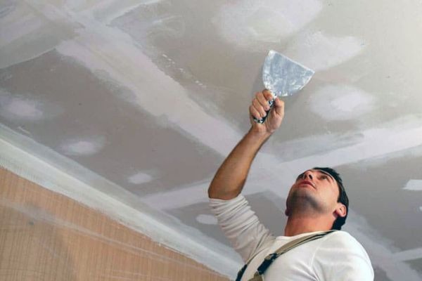 Người đàn ông đang trát bột trét lên trần nhà, cải thiện bề mặt cho nội thất.
