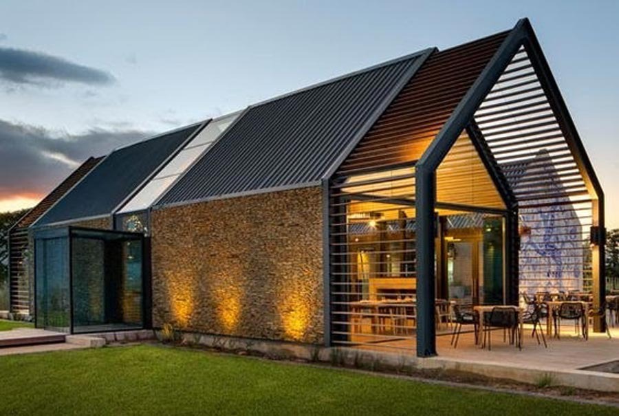 Ngôi nhà hiện đại với kiến trúc mái kim loại và vách kính, nhìn từ bên ngoài lúc hoàng hôn.