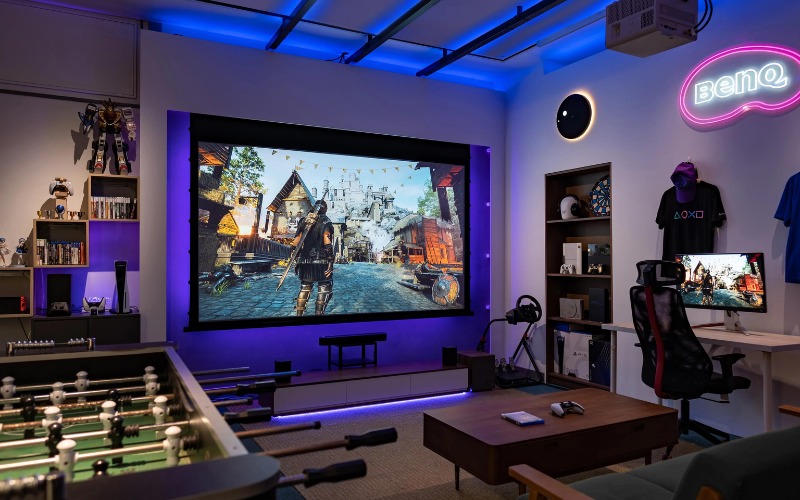 Phòng giải trí hiện đại với màn hình lớn chiếu game, máy tính và đèn neon BenQ.