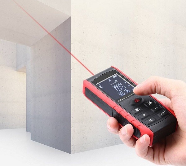 Thiết bị đo laser cầm tay đỏ đang đo khoảng cách đến bức tường bê tông trắng.