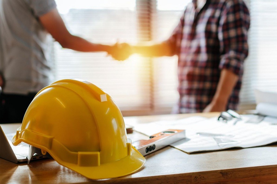 Mũ bảo hộ và hai người bắt tay nhau trong văn phòng, tượng trưng cho hợp tác xây dựng.