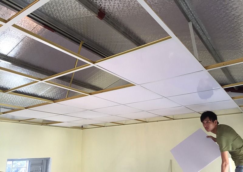 Công nhân lắp đặt trần thạch cao, với khung kim loại và tấm cách nhiệt bên trên.