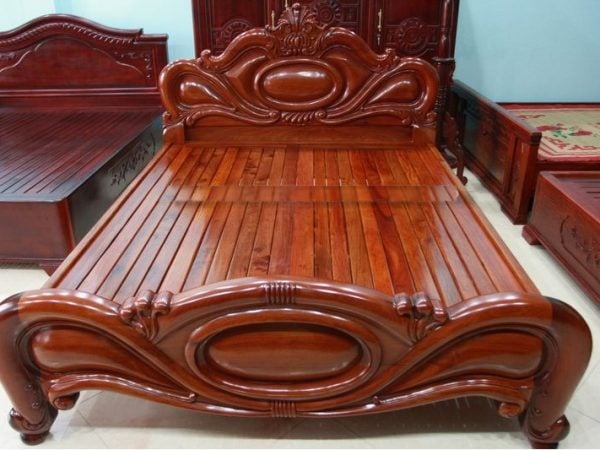 Giường gỗ cổ điển với chạm khắc tinh xảo, chất liệu nâu bóng. Nội thất phòng ngủ sang trọng.