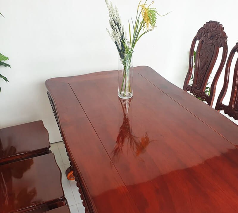 Bàn gỗ nâu bóng trang trí bình hoa, ghế tựa chạm khắc tinh xảo, nội thất sang trọng.