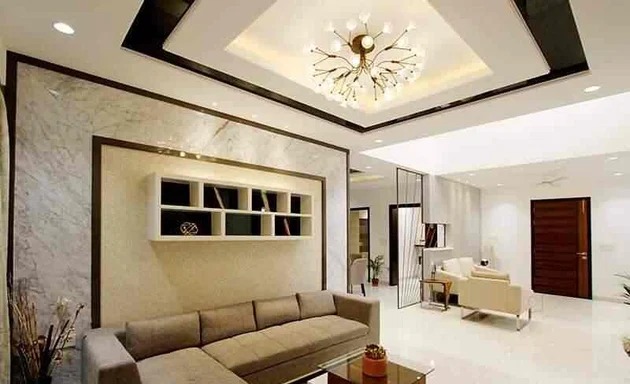 Phòng khách hiện đại với sofa xám, trần đèn chùm và kệ trang trí trên tường đá.