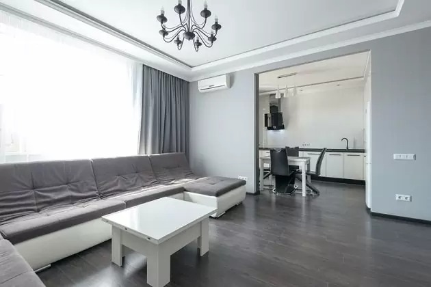 Phòng khách hiện đại với sofa xám, bàn trắng, đèn chùm, sàn gỗ tối và cửa sổ lớn.