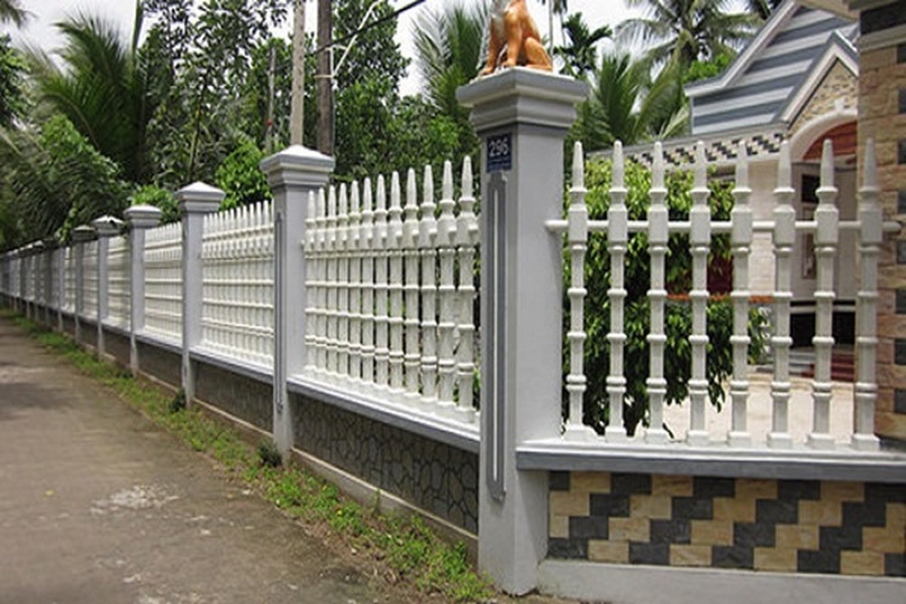 Hàng rào trắng bao quanh ngôi nhà với cây xanh và bầu trời xanh phía sau.