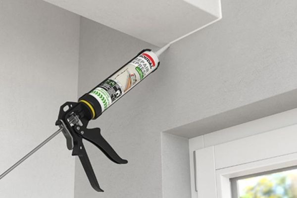 Súng bắn keo silicone đang sử dụng để gắn kín góc trần nhà cạnh cửa sổ.