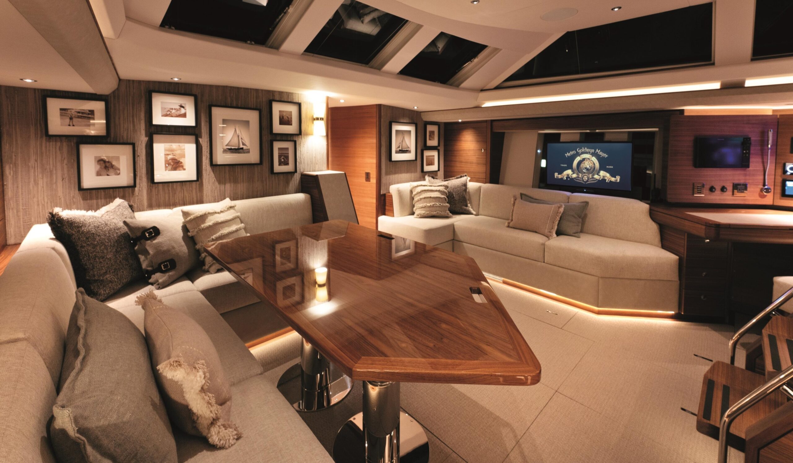 Phòng khách trên du thuyền cao cấp với nội thất sang trọng, bàn gỗ, ghế sofa lớn và trang trí ảnh nghệ thuật tường.