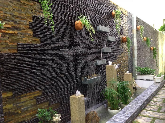 Tường nước trang trí sân vườn với cây xanh và chậu gốm, tạo không gian thư giãn và tự nhiên.