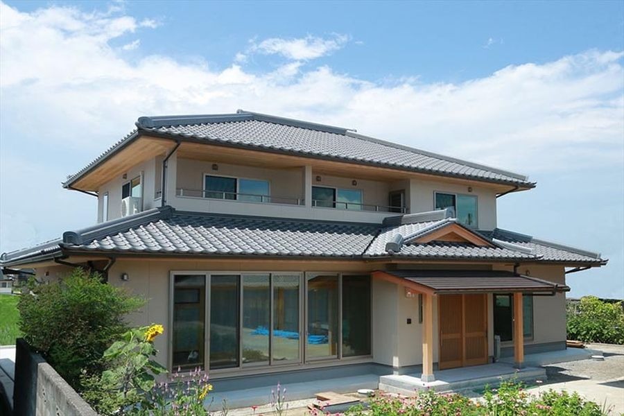 Ngôi nhà truyền thống Nhật Bản với mái ngói xám, vườn cây xanh và bầu trời trong xanh.