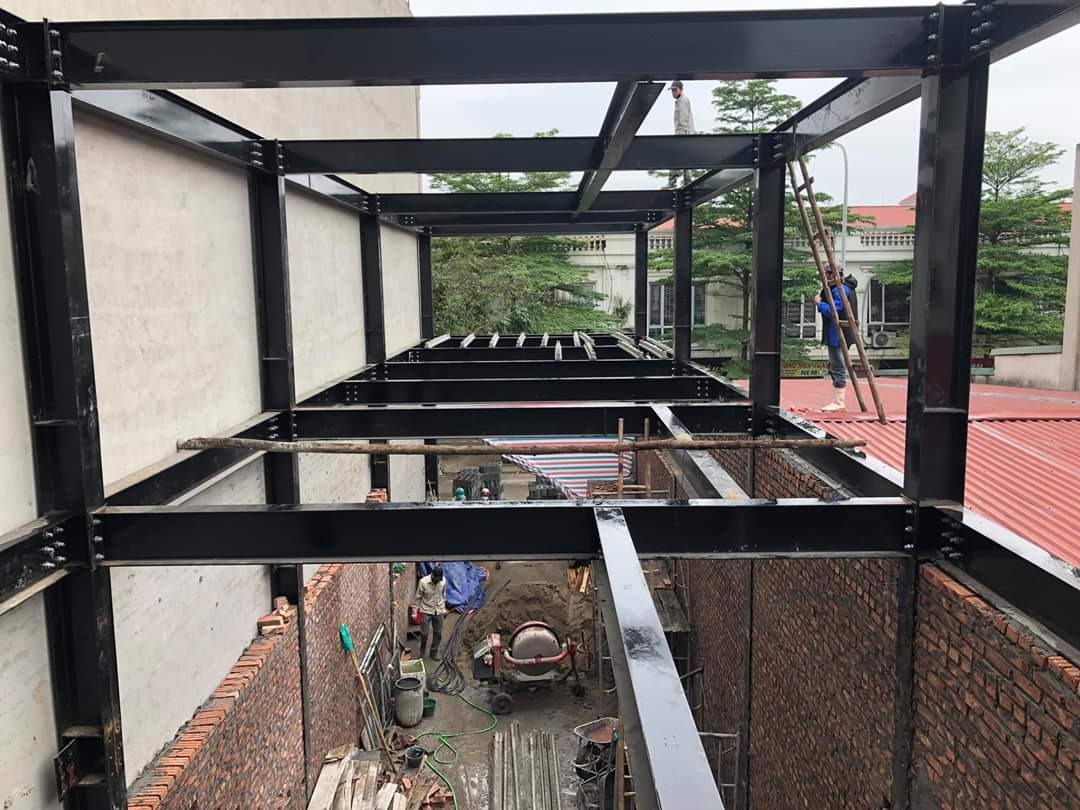 Khung thép xây dựng với công nhân làm việc trên cao bên cạnh tường gạch và thang leo.