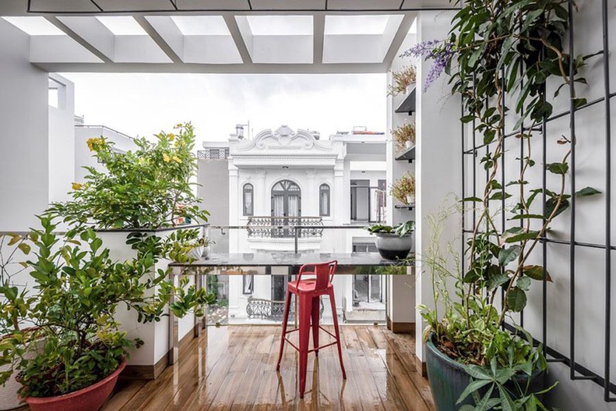 Ban công với bàn dài, ghế đỏ và cây xanh, nhìn ra kiến trúc tân cổ điển của nhà phố.